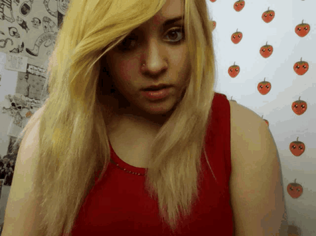 a woman in a red tank top stands in front of a strawberry wallpaper