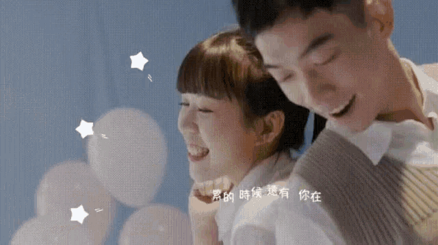 a man and a woman are standing next to each other and smiling with balloons in the background