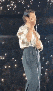 a man is singing into a microphone on a stage while wearing suspenders .
