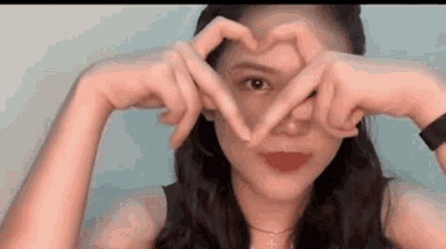 a woman is making a heart with her hands in front of her eyes .