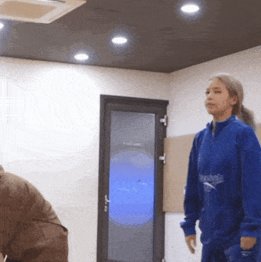 a woman in a blue reebok jacket stands in front of a door