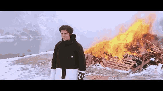a man in a dc jacket stands in front of a pile of burning wood