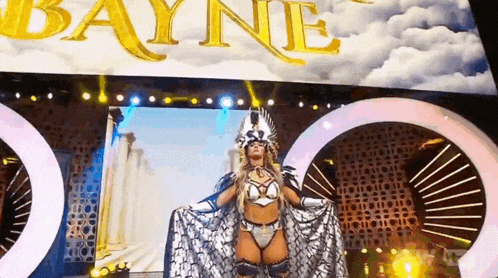 a woman in a costume is standing in front of a large screen that says bayne