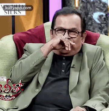 a man in a suit and glasses is sitting on a couch with his hand to his face .