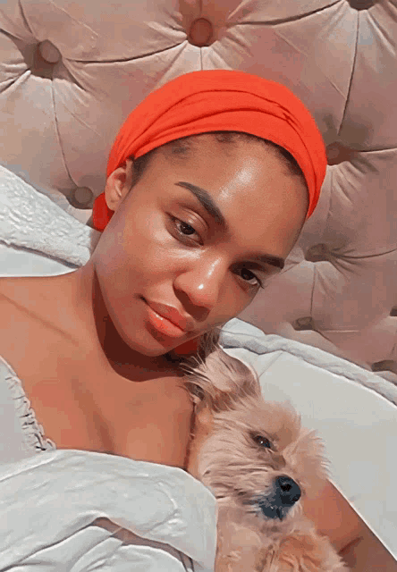 a woman wearing an orange headband is laying on a bed with a dog
