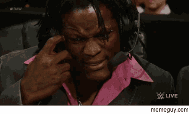 a man wearing headphones and a pink shirt is sitting in front of a microphone on a wrestling show