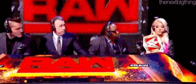 a group of people are sitting in front of a sign that says raw on it .