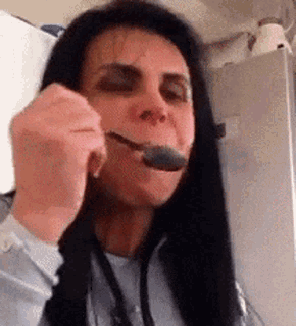 a woman with long black hair is eating something with a spoon in her mouth .