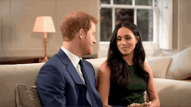 a man in a suit and tie sits next to a woman in a green dress on a couch