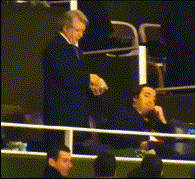 a man in a suit sits in a stadium watching a game