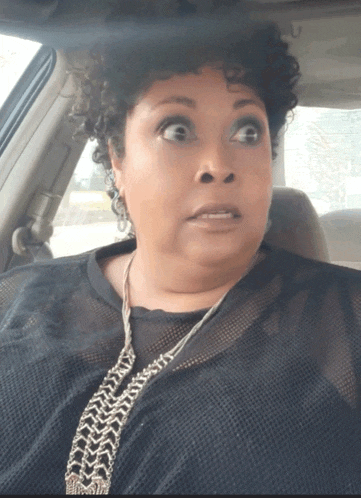 a woman with curly hair is sitting in a car and making a funny face