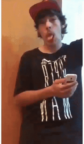a man wearing a hat and a black shirt with the word jam on it is looking at his phone