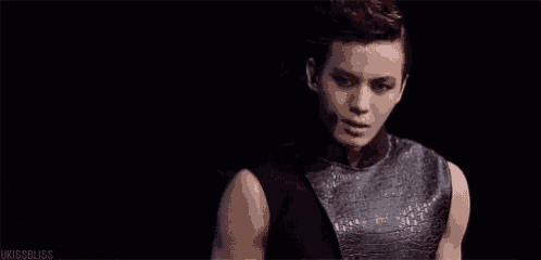 a young man wearing a black sleeveless top and a microphone is standing in a dark room .