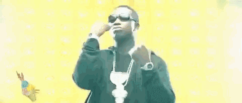 a man wearing sunglasses and a necklace is dancing in front of a yellow background .