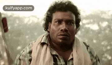a man with curly hair and a towel around his neck is looking at the camera with a surprised look on his face .