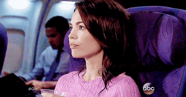 a woman in a pink sweater is sitting in a purple seat on an airplane with the abc logo visible