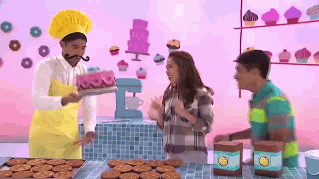 a man in a chef 's hat is holding a tray of donuts in front of two people