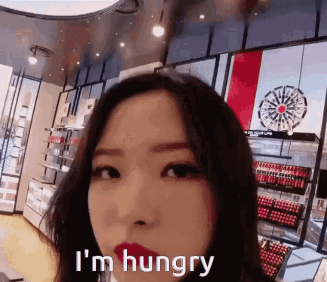 a woman wearing red lipstick is standing in a store and says i 'm hungry .