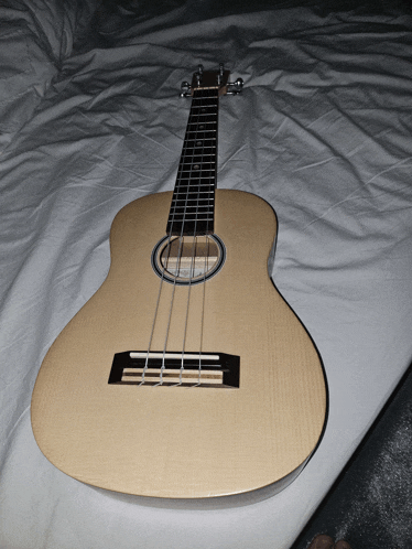 a ukulele is sitting on a bed with a white sheet