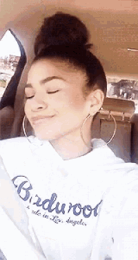 a woman wearing a birdwood hoodie is sitting in a car with her eyes closed