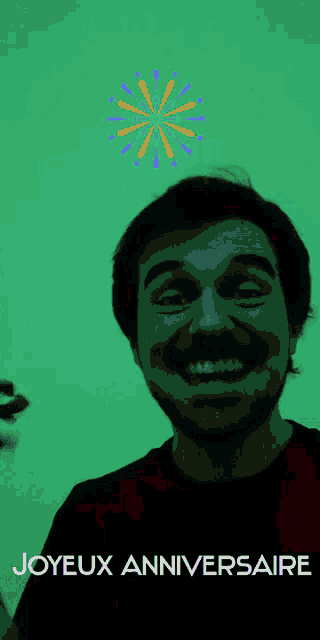 a man with a beard is smiling in front of a green background with joyeux anniversaire written on it