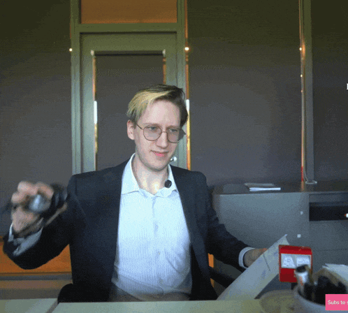 a man in a suit and glasses is sitting at a desk with a red box that says ' subscribe ' on it