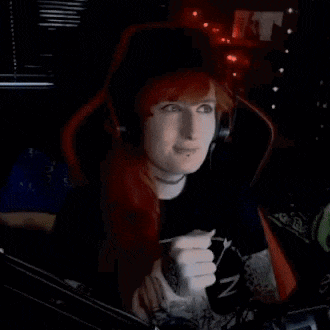 a woman with red hair is wearing headphones and a choker while sitting in a gaming chair .