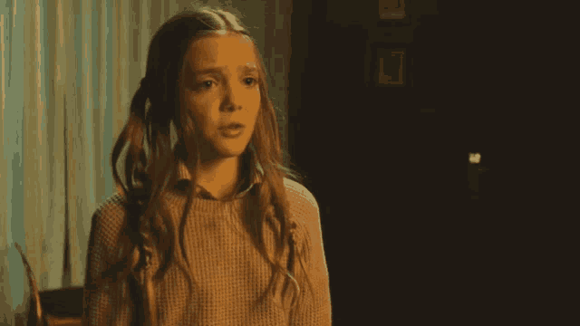 a young girl with pigtails is wearing a sweater and making a surprised face
