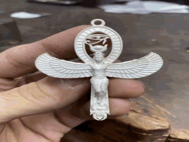 a person is holding a white ankh with wings and a snake on it