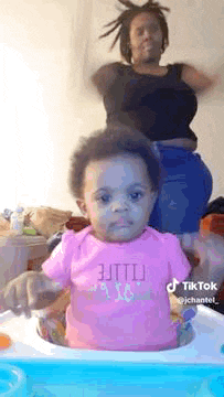 a baby is sitting in a high chair while a woman stands behind it .