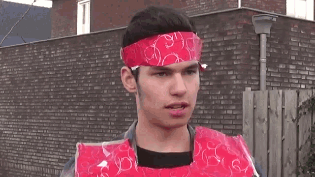a man wearing a red bandana on his head stands in front of a brick building