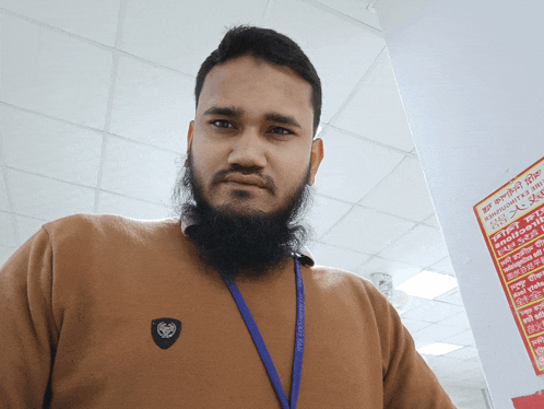 a man with a beard and a lanyard around his neck stands in front of a sign that says ' a '