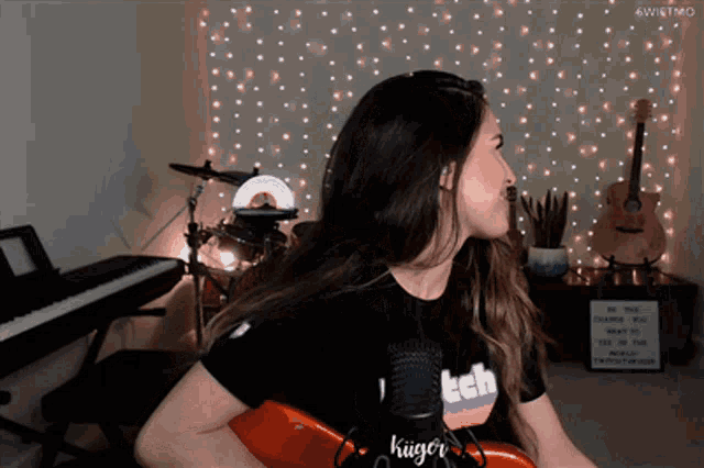 a woman wearing a shirt that says twitch on it is playing a guitar