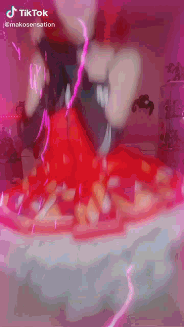 a woman in a red dress is dancing in a room with a pink background .