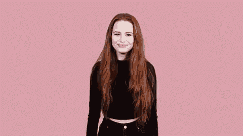 a woman with long red hair is wearing a black sweater and black jeans and smiling .