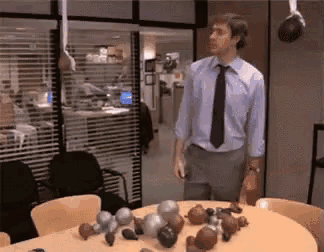 a man in a blue shirt and tie is standing in front of a table filled with christmas ornaments .