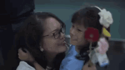 a woman is hugging a little girl who is holding a bouquet of flowers in her hand .