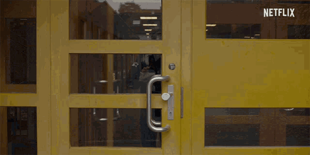a man in a black jacket stands in front of a yellow door with netflix written on it