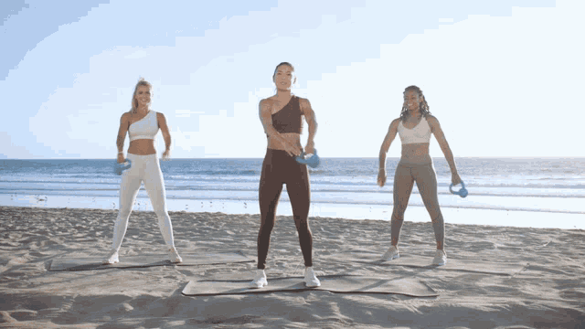 three women doing exercises on a beach with dumbbells
