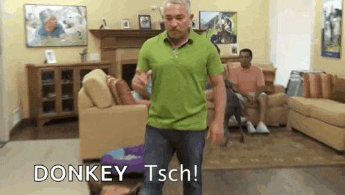 a man in a green shirt is dancing in a living room with a group of people sitting on couches .