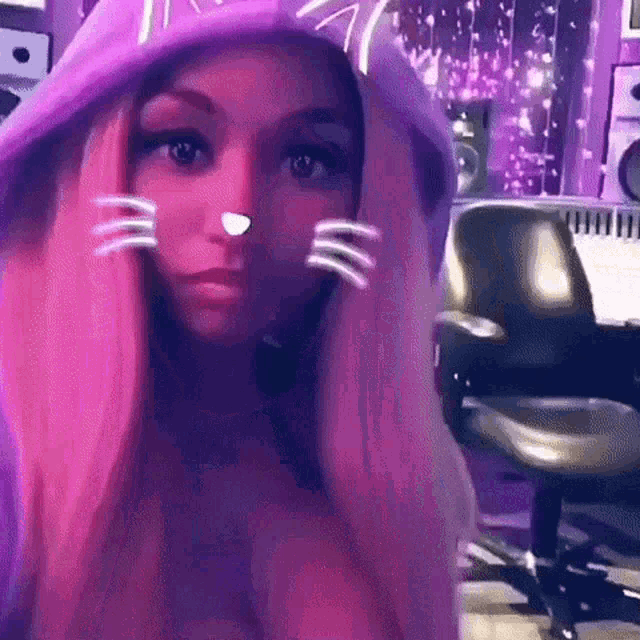 a girl with pink hair is wearing a purple cat hoodie and a cat nose .