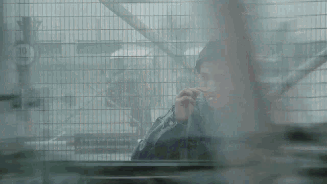 a man in a purple jacket is smoking a cigarette behind a wire fence