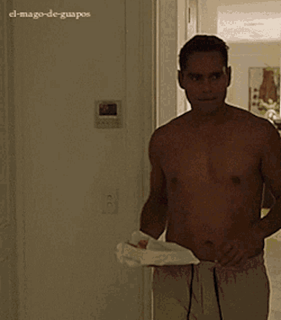 a shirtless man is holding a towel in front of a wall that says el-mago-de-guapos