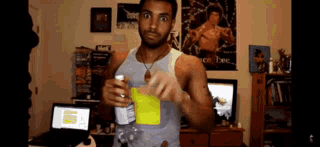 a man is holding a bottle of water in front of a laptop and a bruce lee poster