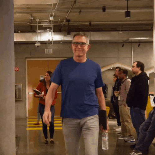 a man in a blue shirt is walking down a hallway holding a water bottle