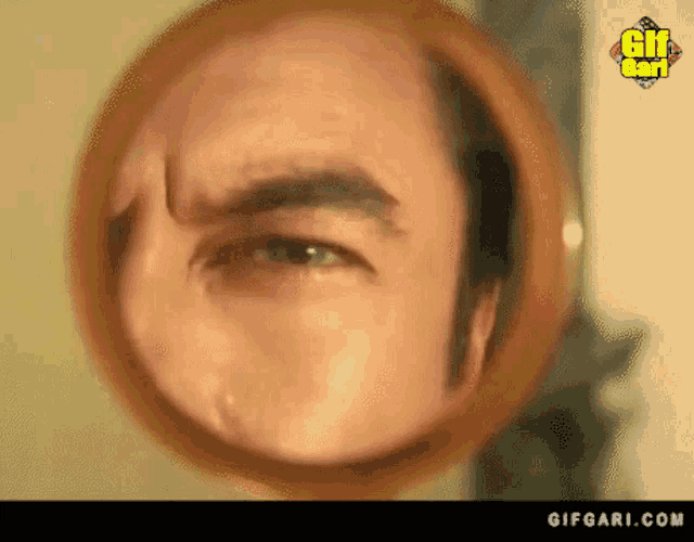 a close up of a man 's face in a round mirror with gifgari.com written on the bottom