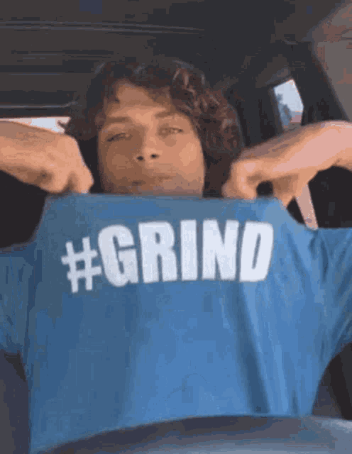 a man is sitting in a car wearing a blue shirt that says # grind .