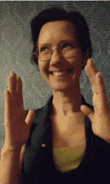 a woman wearing glasses is smiling and holding her hands up in front of her face