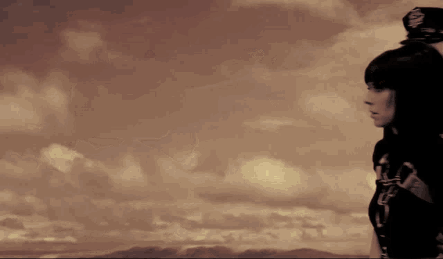 a woman stands in front of a cloudy sky with mountains in the background