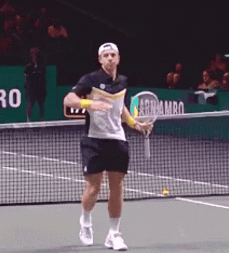 a man is holding a tennis racquet on a tennis court in front of a net .